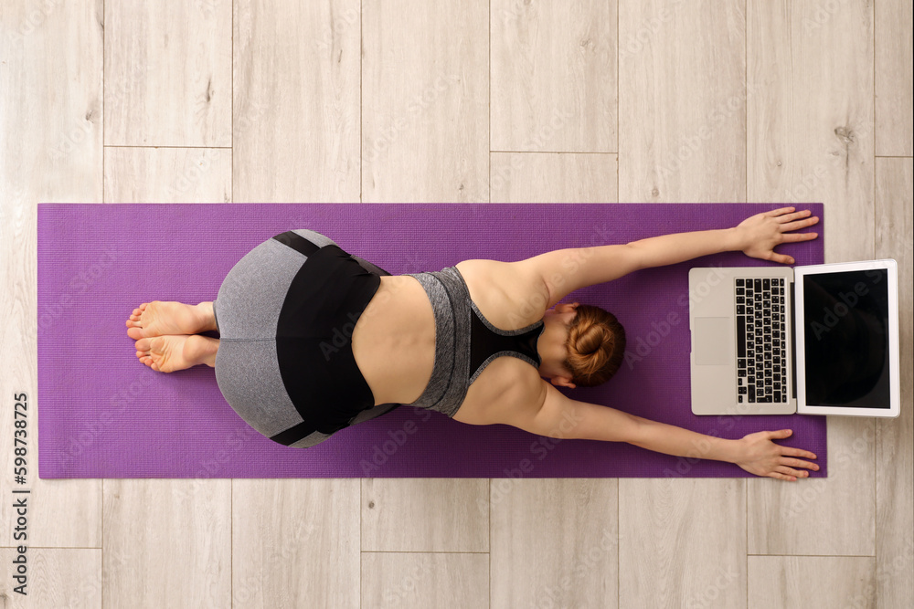 Sporty young woman with laptop doing yoga in gym, top view