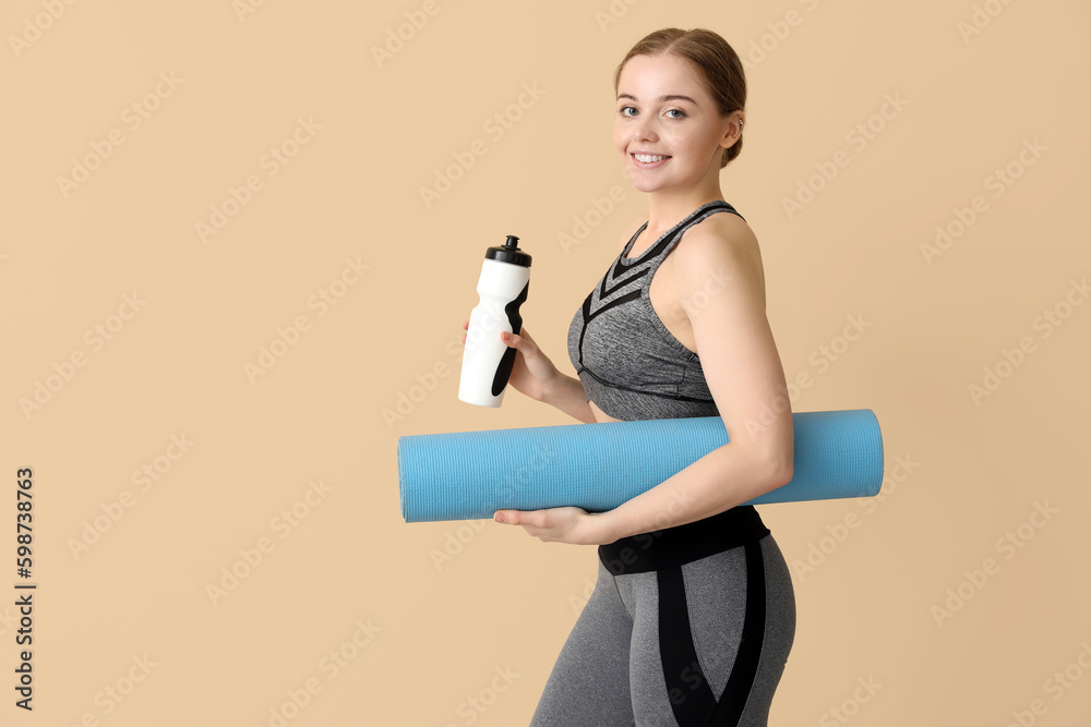 Sporty young woman with yoga mat and bottle of water on beige background