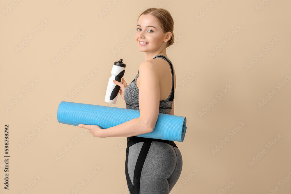 Sporty young woman with yoga mat and bottle of water on beige background