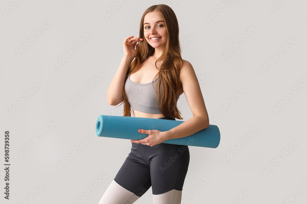 Sporty young woman with yoga mat on grey background