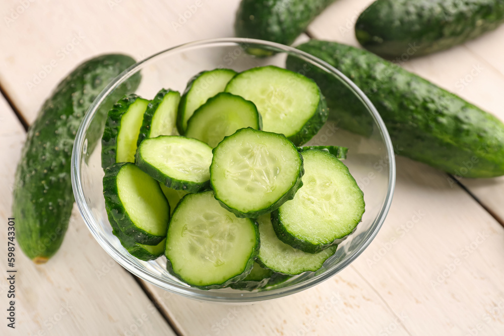 Bowl with pieces of fresh cucumber on light wooden background