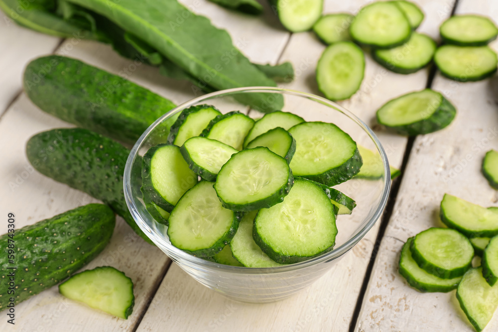 Bowl with pieces of fresh cucumber on light wooden background