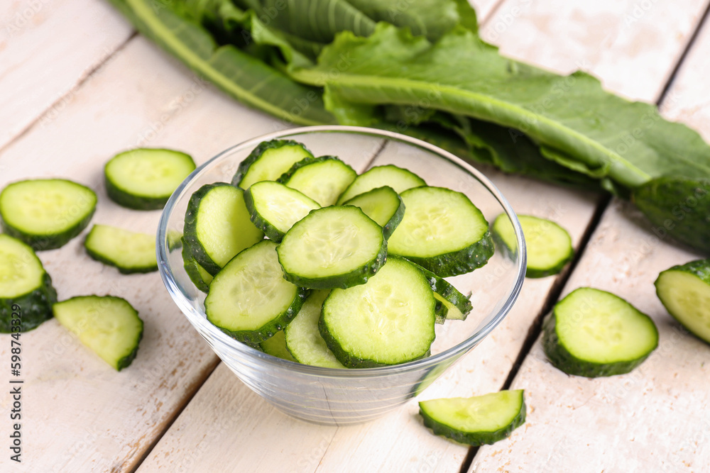 Bowl with pieces of fresh cucumber on light wooden background