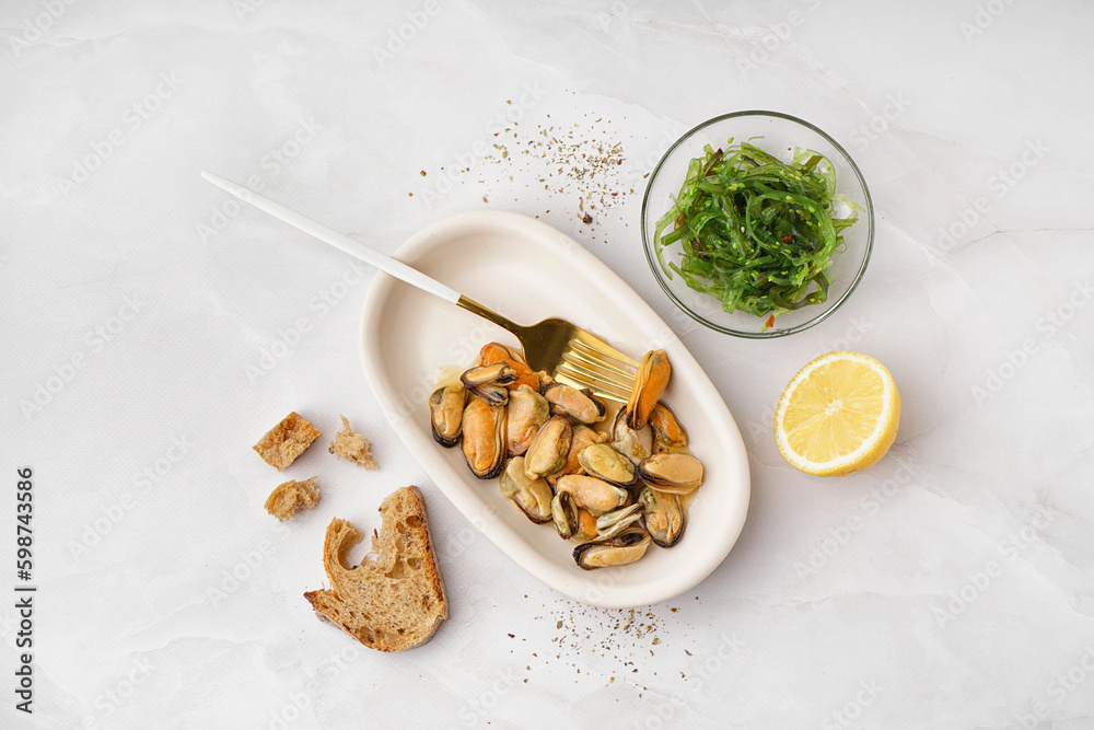 Plate with pickled mussels and bowl of seaweed salad on white background