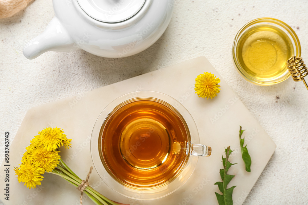 Glass cup of healthy dandelion tea with honey and teapot on white background