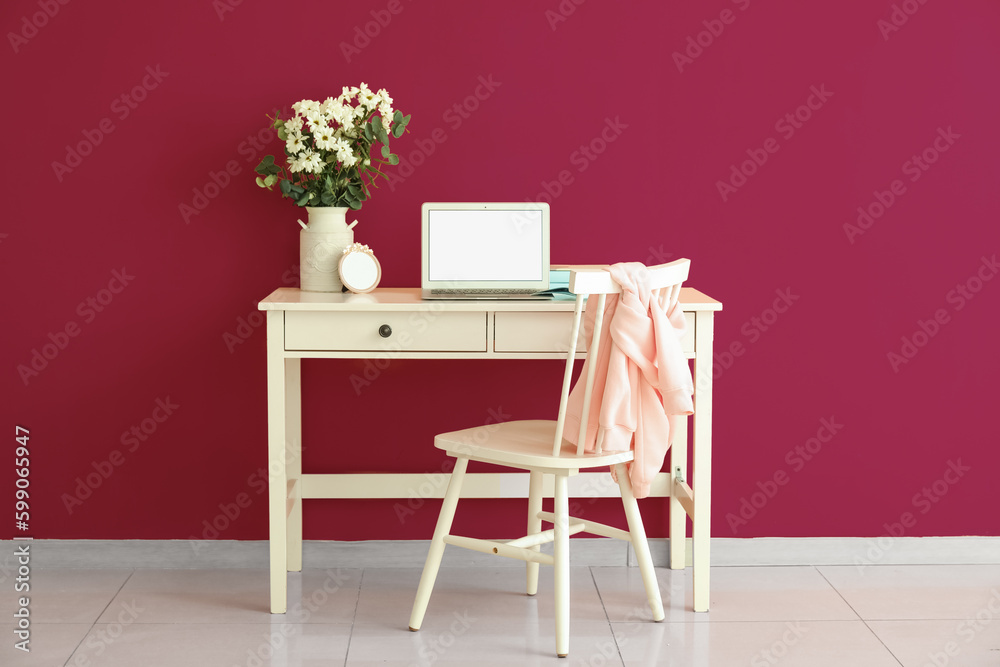 Modern workplace with laptop and daisy flowers in vase near pink wall