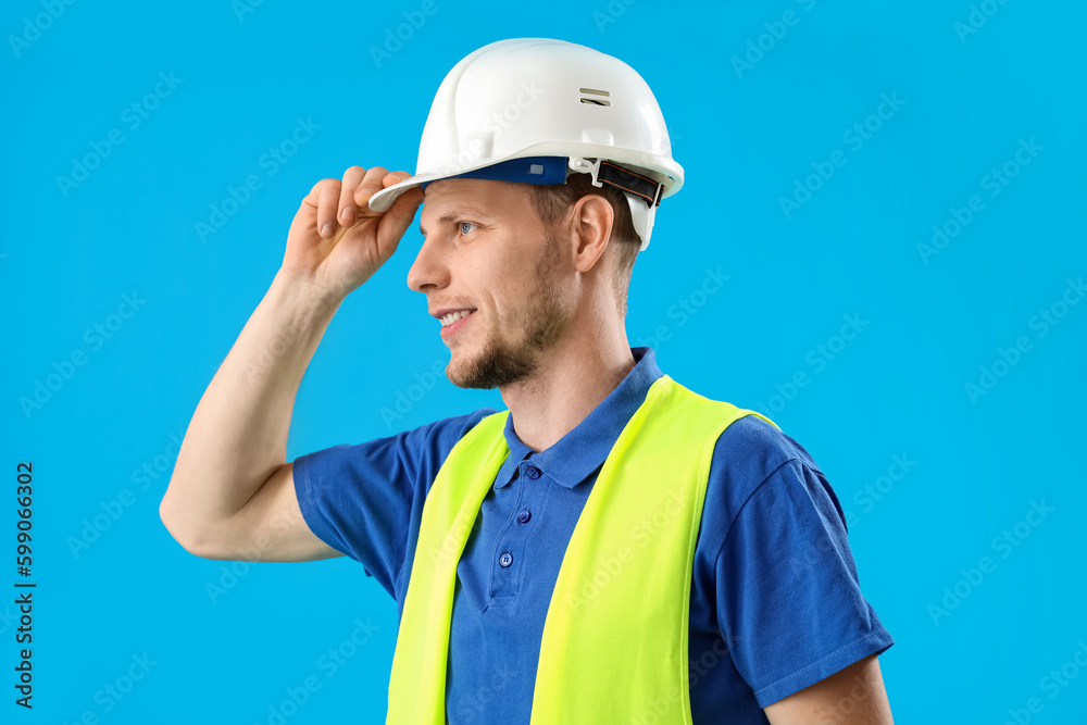 Male worker in vest and hardhat on blue background