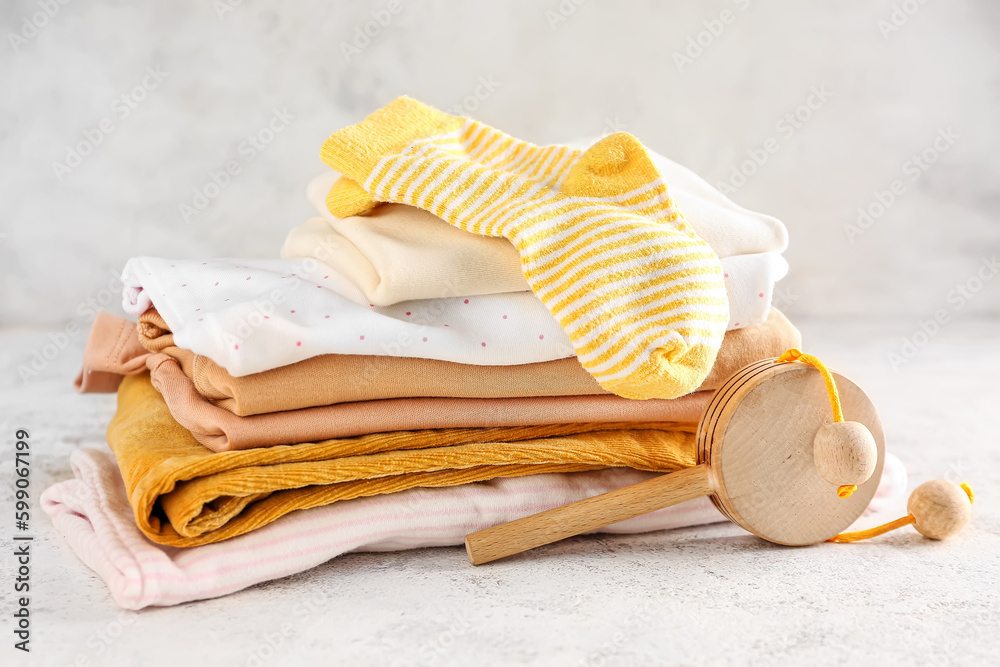 Stack of baby clothes and wooden toy on light background