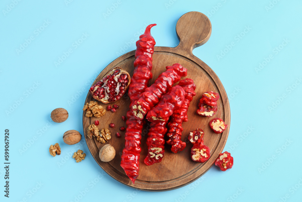 Wooden board with tasty churchkhela, walnuts and pomegranate on color background