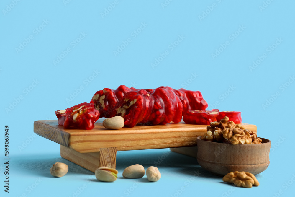 Wooden boARD WITH tasty churchkhela and nuts on color background