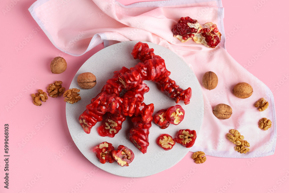 Board with tasty churchkhela and nuts on pink background