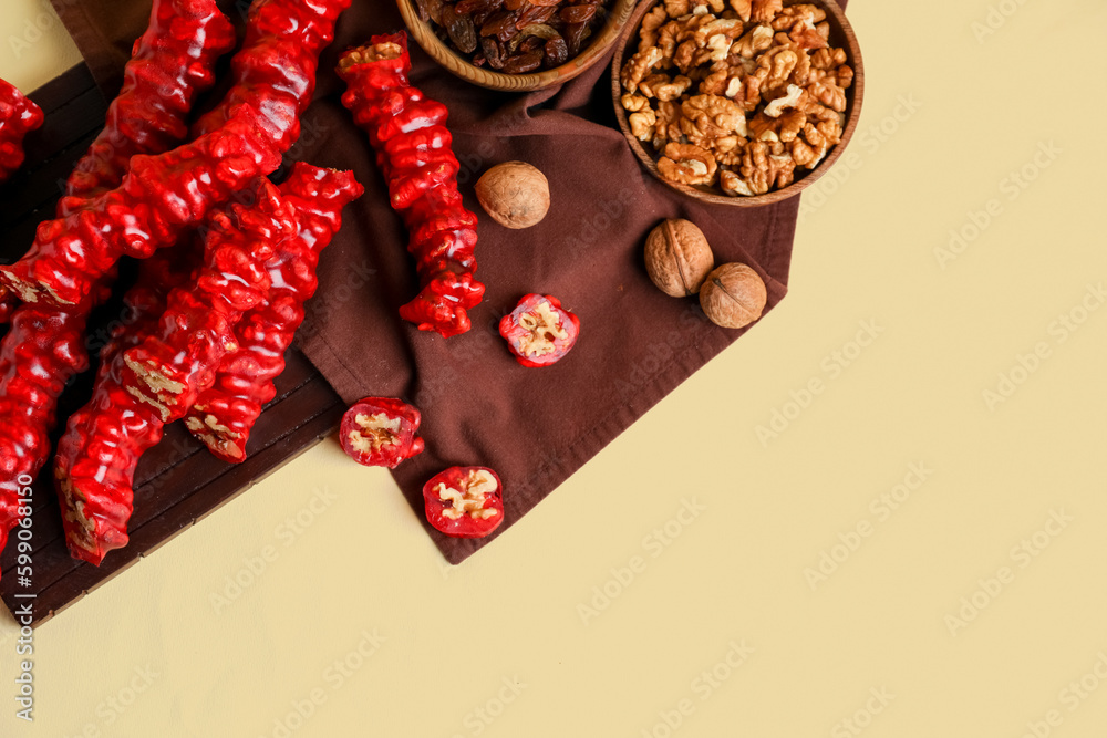 Wooden board with tasty churchkhela and walnuts on color background