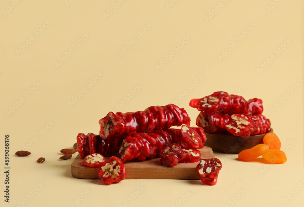 Wooden board with tasty churchkhela, almond nuts and dried apricots on color background