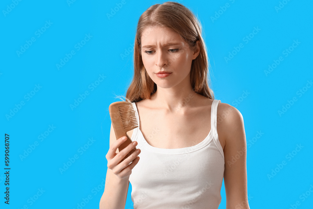 Upset young woman with comb and fallen down hair on blue background