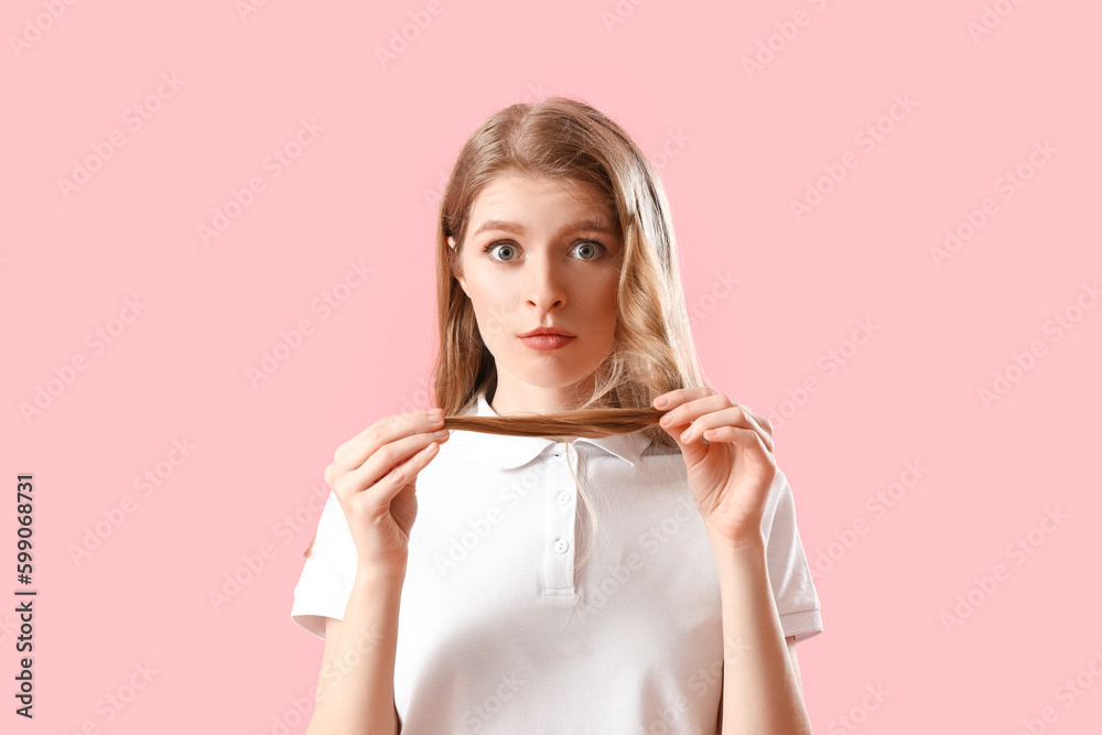 Worried young woman with hair loss problem on pink background