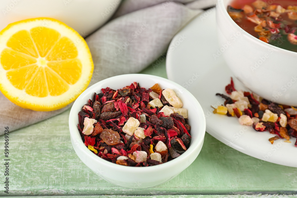 Bowl with dried fruit tea and lemon on green wooden table, closeup