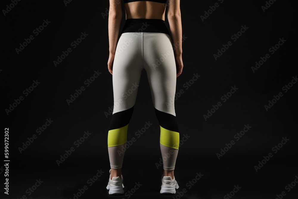 Sporty young woman in leggings on black background, back view