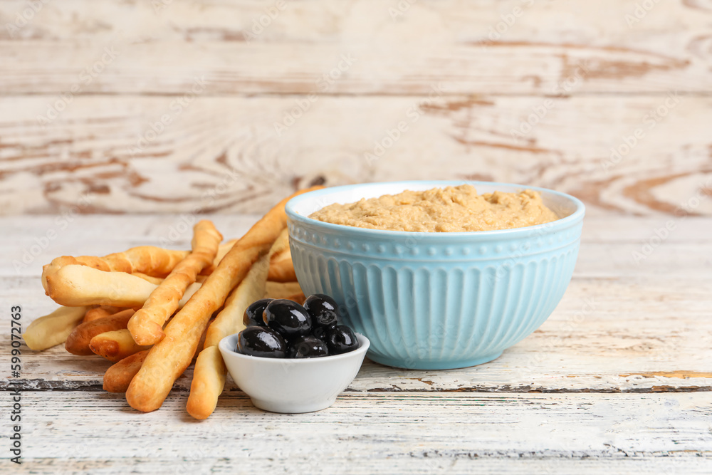 Bowl with tasty hummus and Italian Grissini on light wooden background