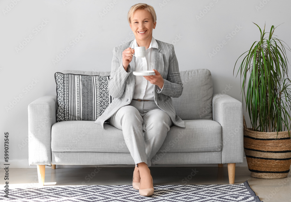 Mature businesswoman drinking coffee while sitting on sofa in office