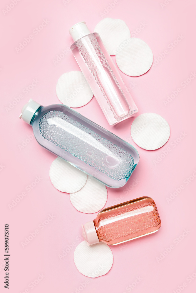 Bottles of micellar water with cotton pads on pink background