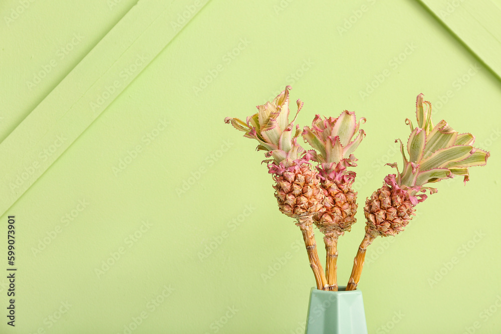 Vase with decorative pineapples near green wall, closeup