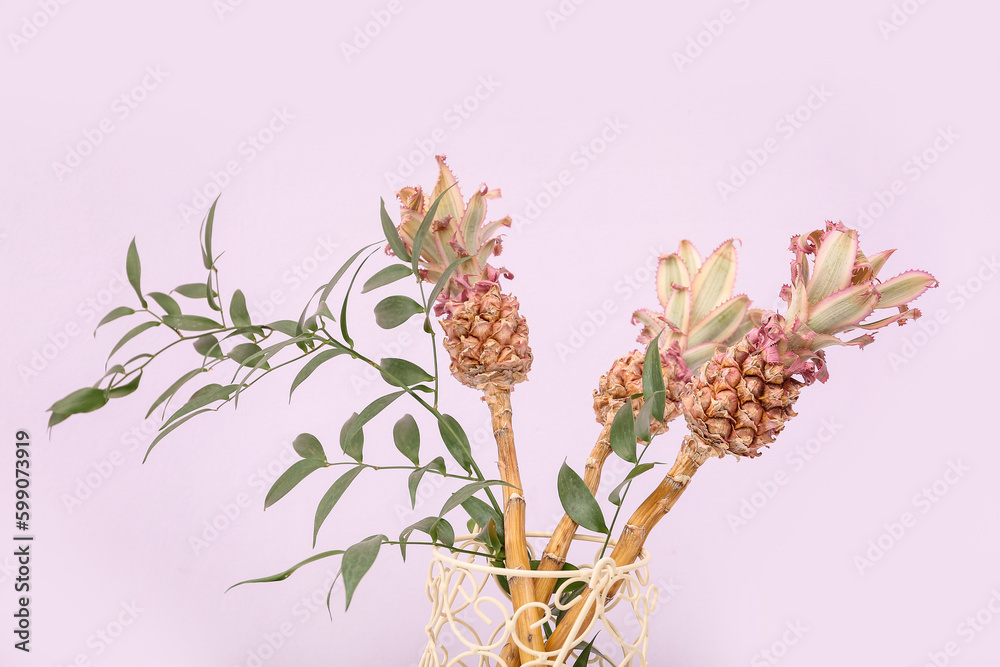 Vase with decorative pineapples and plant branches on lilac background, closeup