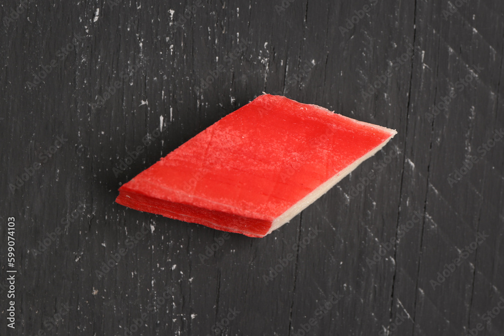 Piece of tasty crab stick on dark wooden background, closeup