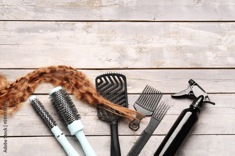 Curly ginger hair with brushes and spray on light wooden background