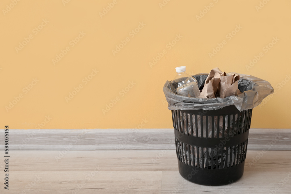 Plastic trash bin with different garbage near yellow wall