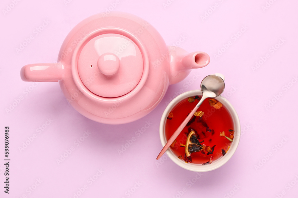 Ceramic teapot with cup of fruit tea on lilac background