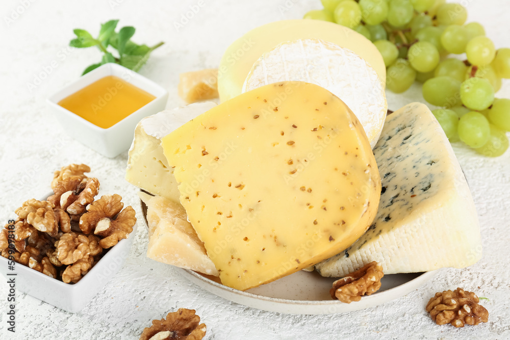 Plate with different types of cheese and nuts on light background