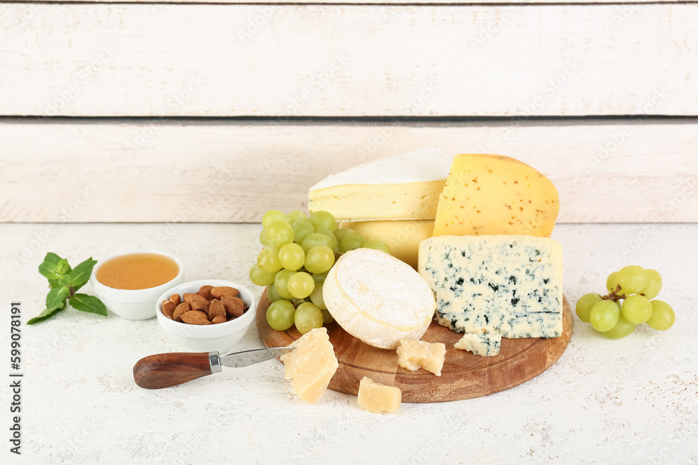 Wooden board with different types of cheese, grapes and nuts on table