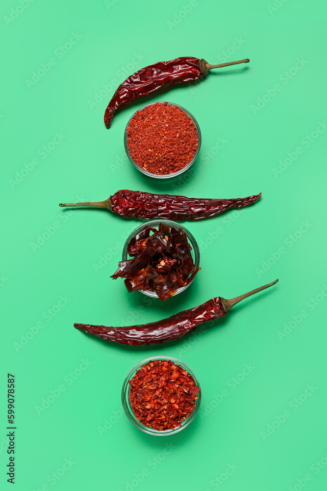 Dry hot chili peppers and bowls of spices on green background