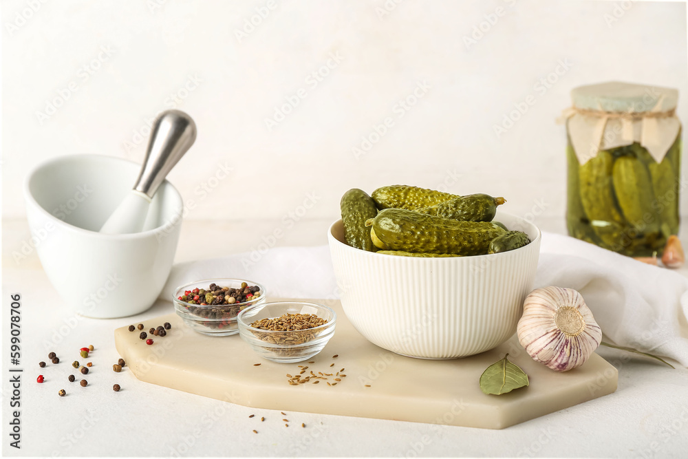 Mortar and board with bowl of canned cucumbers on white table