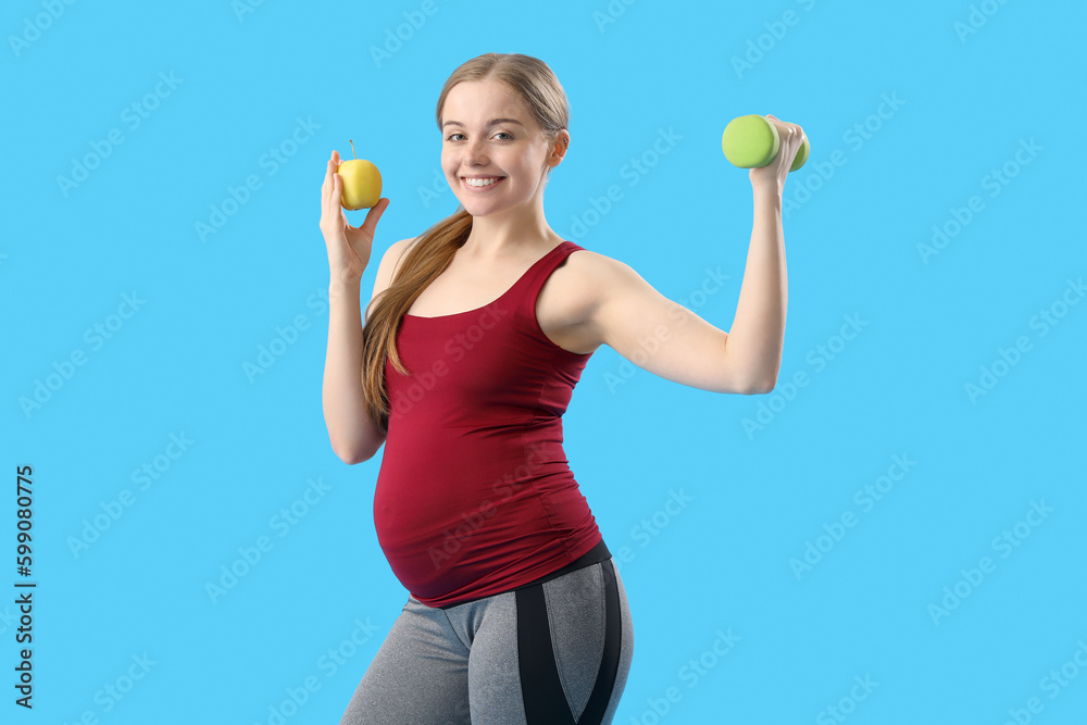 Sporty pregnant woman with apple and dumbbell on blue background