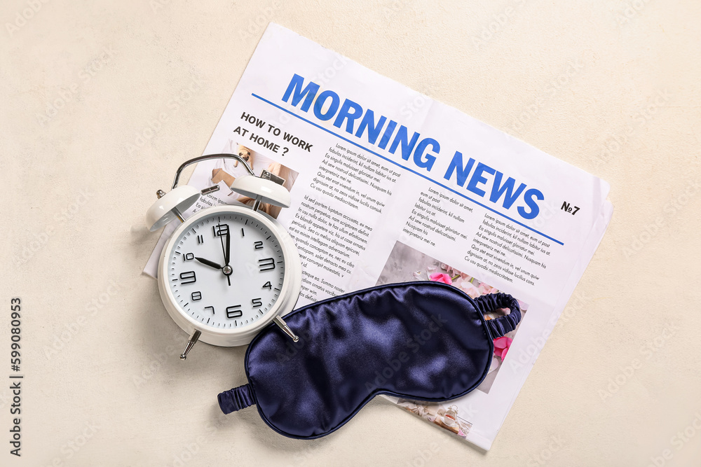 Alarm clock with sleep mask and newspaper on light background