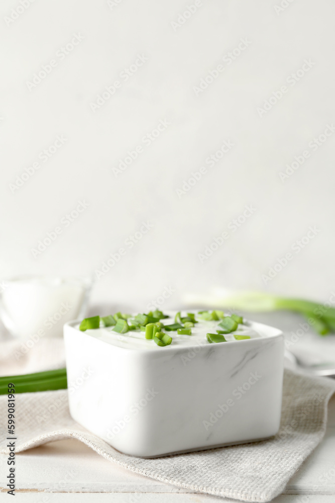 Square bowl with sour cream and sliced green onion on white wooden table near wall