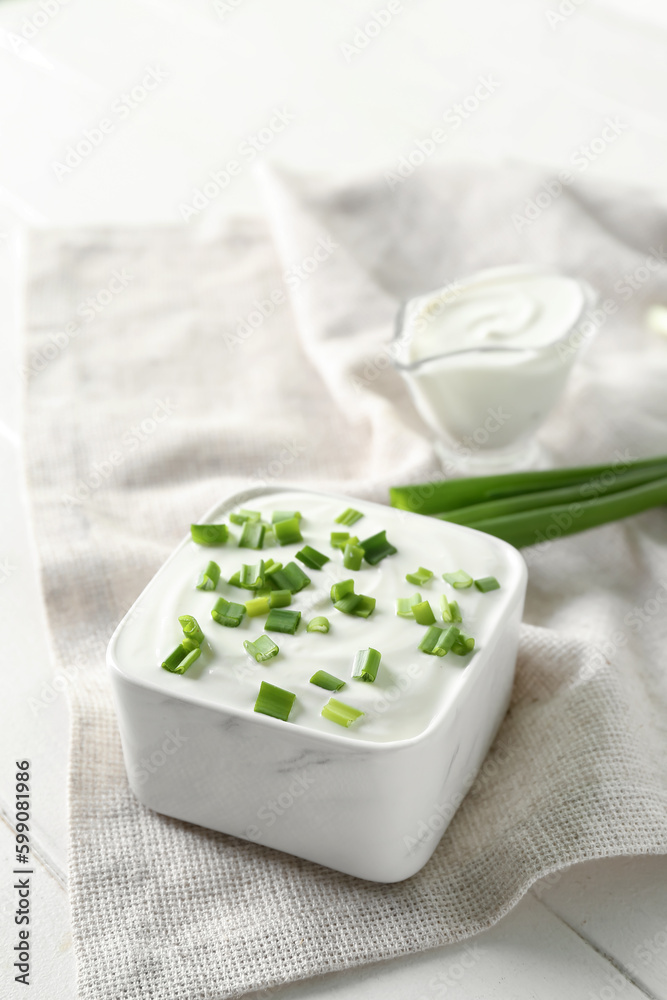 Square bowl with sour cream and sliced green onion on white wooden table