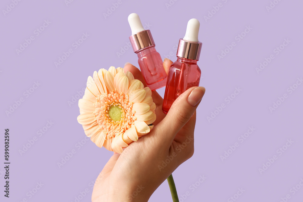 Hand holding bottles of essential oil and flower on lilac background