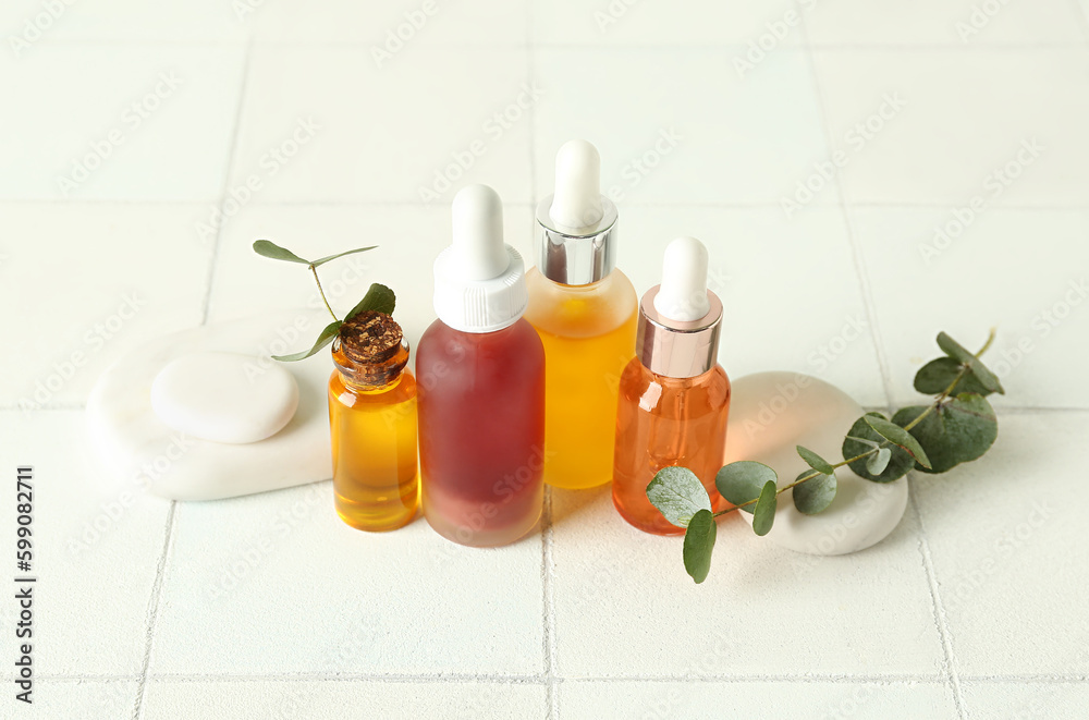 Composition with bottles of cosmetic oil, spa stones and eucalyptus branch on white tile