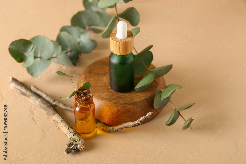 Bottles of cosmetic oil with eucalyptus branch on orange background