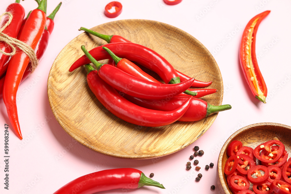 Tied fresh chili with plates of hot peppers on pink background