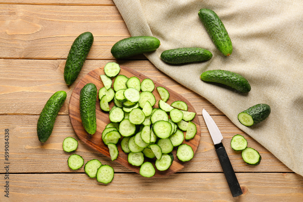 Board with fresh cut cucumbers on wooden background