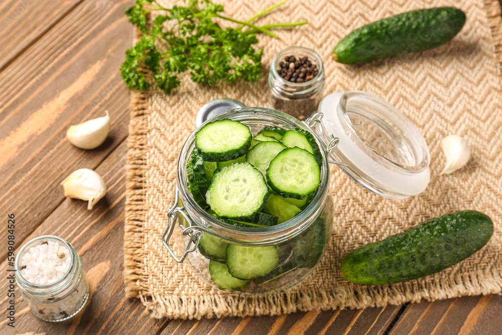 Jar with fresh cut cucumbers and spices on wooden background