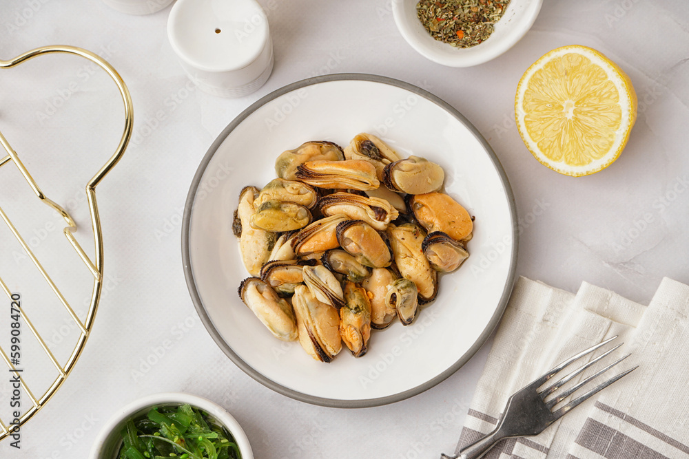 Plate with pickled mussels and bowl of seaweed salad on white background