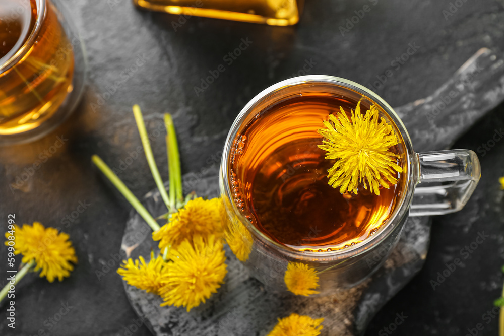 Board with glass cups of healthy dandelion tea on black background