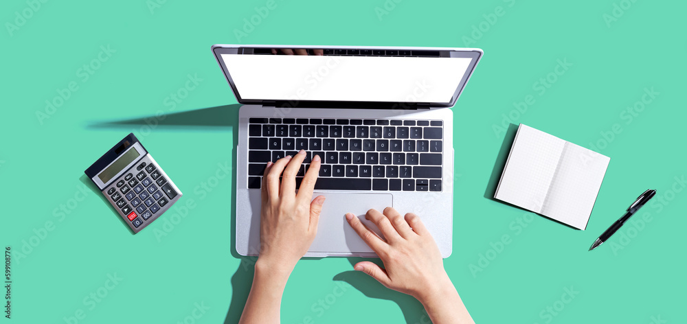 Person using a laptop computer with a notebook and a calculator