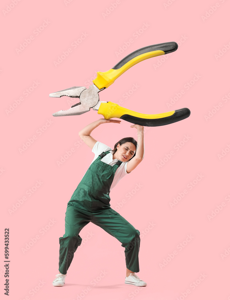 Female worker with big heavy pliers on pink background