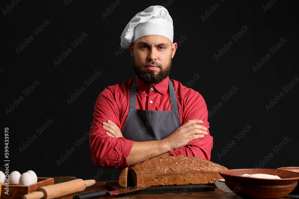 Male baker at table with rye bread on dark background