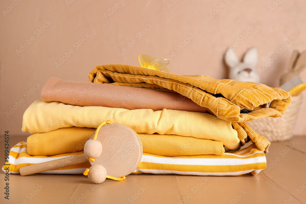 Stack of baby clothes, pacifier and toy on color wooden background